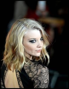 a woman with blonde hair and blue eyes is looking at the camera while wearing a black dress