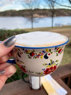 a hand holding a cup with white liquid in it on top of a wooden table