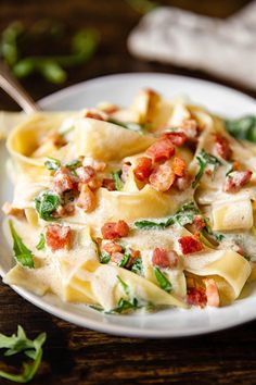 a white plate topped with pasta covered in bacon and spinach