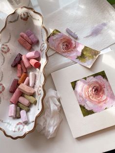 some pink flowers are in a bowl and on a table next to other art supplies