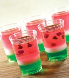 four shot glasses filled with liquid on top of a wooden table