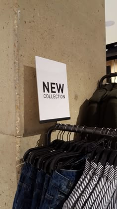 clothes hang on racks in front of a sign that says new collection next to it