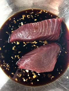 two pieces of raw fish in a bowl with some seasoning on the side and sprinkles