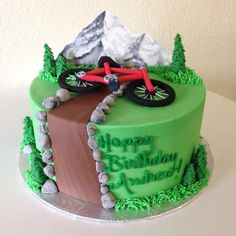 a green birthday cake with a bicycle on it's top and mountains in the background