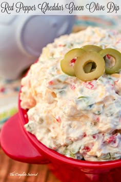 red pepper cheddar green olive dip in a red bowl with an olive on top