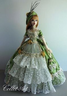 a doll is wearing a green dress and hat with flowers on the skirt, while standing in front of a white wall