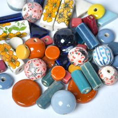 there are many different colored beads on this white table top, including one with an orange flowered design