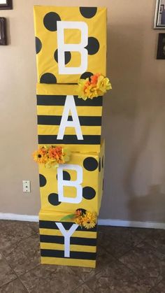 a yellow and black striped baby sign with flowers on the bottom, hanging from a wall