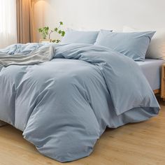 a bed with blue sheets and pillows in a room next to a lamp on a wooden floor