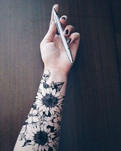 a woman's arm with flowers on it and a pen in the other hand