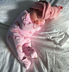 a baby laying on top of a white bed wearing a pink hat and sleeping bag