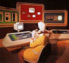 a woman sitting at a desk in front of a control panel with buttons on it