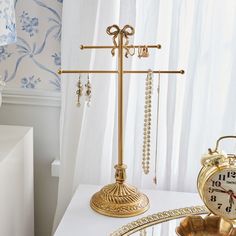 a gold clock sitting on top of a table next to a golden stand with jewelry hanging from it