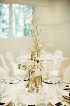 an elegant centerpiece with branches and flowers sits atop a table set for a formal function