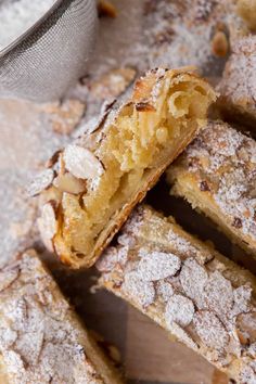 several pieces of dessert sitting on top of a wooden cutting board with powdered sugar