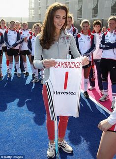 a woman holding up a white shirt with the number 1 on it while standing in front of a group of children