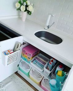 a kitchen sink under a counter next to a white cabinet with lots of containers and utensils