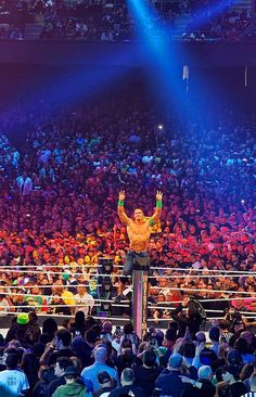 a man standing on top of a metal pole in front of a crowd at a wrestling match