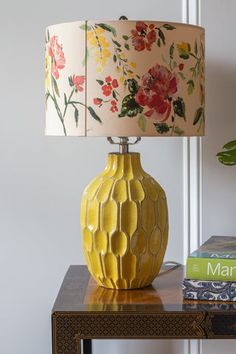 a yellow vase sitting on top of a wooden table next to a book and lamp