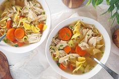 two bowls of chicken noodle soup with carrots and parsley on the side