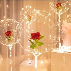 three wine glasses with roses in them sitting on a table next to candles and flowers