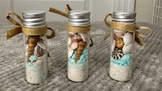 three glass bottles filled with sand and seashells on top of a carpeted floor