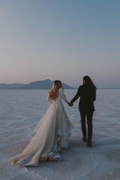 a bride and groom holding hands in the middle of an empty salt flat with mountains in the background