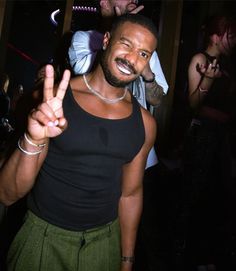 a man making the peace sign with his hand and other people behind him at a party