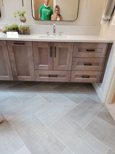 a man and woman standing in front of a bathroom vanity with grey tile on the floor