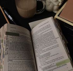 an open book sitting on top of a table next to a cup of coffee and a pen