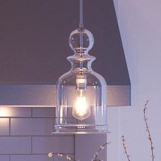 a clear glass light hanging from a ceiling fixture in a kitchen with white tiles on the wall