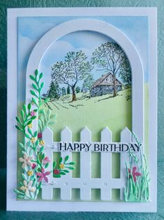 a happy birthday card with a white picket fence and flowers on the outside, in front of a green background