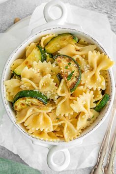 pasta with zucchini and spinach in a white bowl on top of a napkin