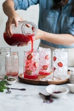 someone pouring strawberry juice into small glasses on a cutting board with ice and strawberries