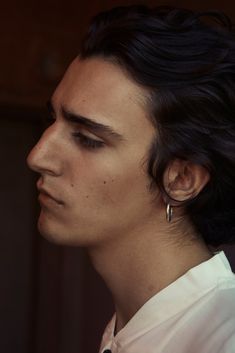 a man with black hair and earrings on his head looking off to the side, wearing a white shirt