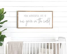 a white crib with a wooden sign that says how wonderful life is now, grow in the world