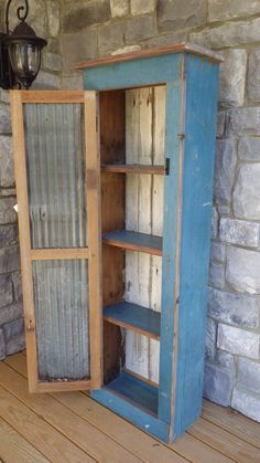 an old blue cabinet is sitting on a wooden floor next to a brick wall and lamp