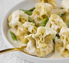 a white bowl filled with pasta and broccoli on top of a table next to a fork