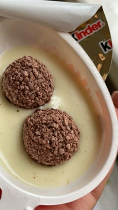 two chocolate cookies are in a white bowl with yogurt on the side,