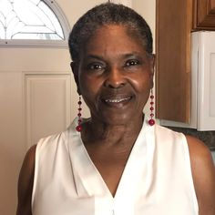 an older woman in a white top standing in front of a door and smiling at the camera