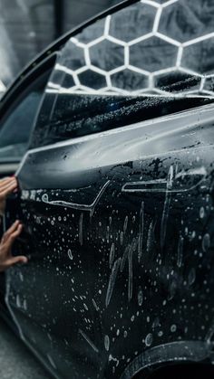 a woman is leaning on the hood of a car with her hand in the door handle