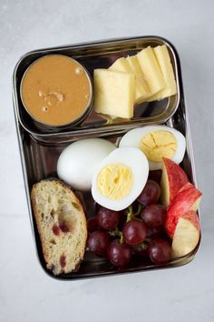 an open lunch box with eggs, cheese, fruit and bread on it's side