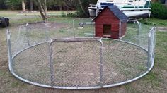 a dog house in the middle of a fenced off yard with a boat behind it