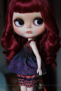 a close up of a doll with long red hair and big eyes, wearing a purple dress