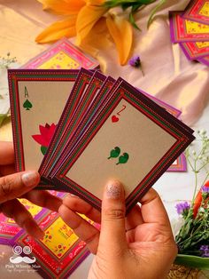 a person holding four playing cards in their hand with flowers on the table behind them