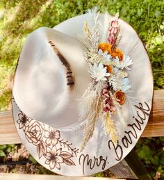 a white hat with flowers on it sitting on a wooden bench in front of trees