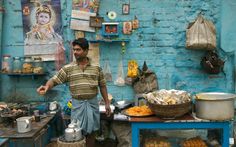 a man standing in front of a blue brick wall with food on the table and other items