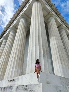 a woman sitting on the side of a tall building next to some white pillars with columns