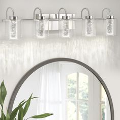 a bathroom vanity with three lights and a mirror on the wall next to a potted plant