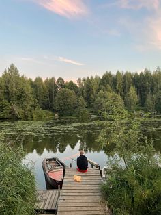 a person sitting on a dock next to a small boat in the middle of a lake